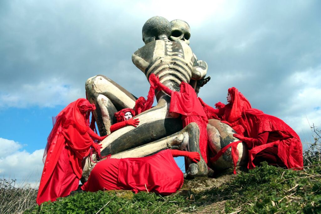 Red Rebels gather around a statue of two giant skeletal figures.
Photo by Feng Ho