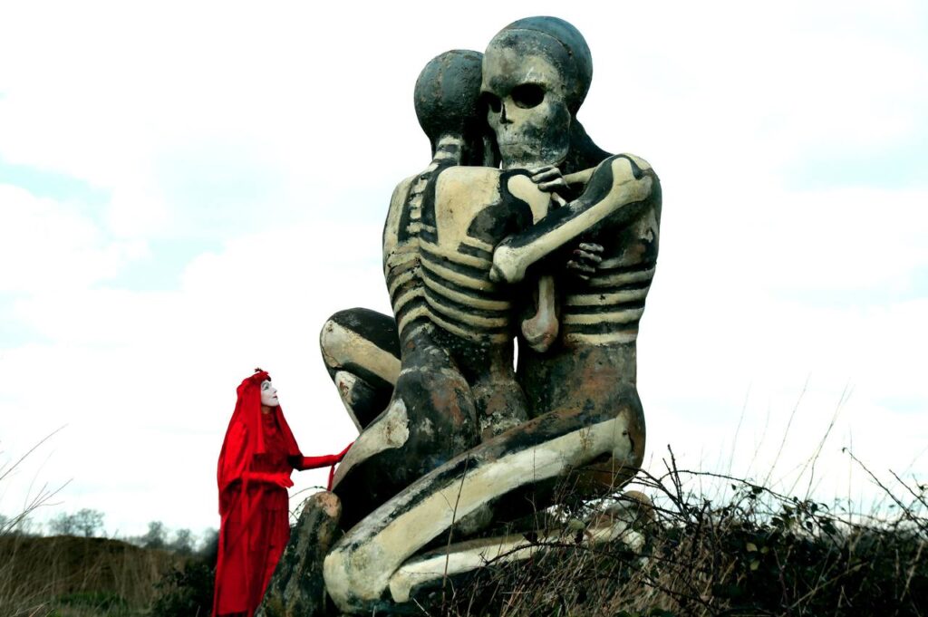 A Red Rebel stands at the base of The Nuba Survival, a giant sculpture of two skeletal figures.