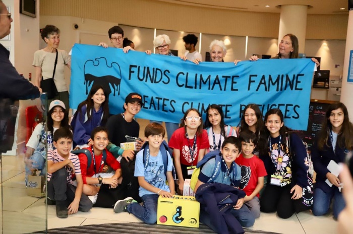 Extinction Rebellion protestors hold a banner showing Barclays Funds Climate Famine, Barclays Create Climate Refugees
A group of schoolchild sit in front.